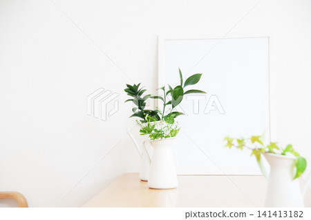White potted plants in a white vase, displayed against a white wall and wooden table. White potted plants in a white vase, displayed against a white wall and wooden table. 141413182