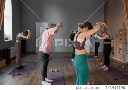 Young caucasian woman doing roll down exercise in a pilates bright studio. Their workout focuses on core strength and flexibility in a modern fitness environment Young caucasian woman doing roll down exercise in a pilates bright studio. Their workout focuses on core strength and flexibility in a modern fitness environment 141413198