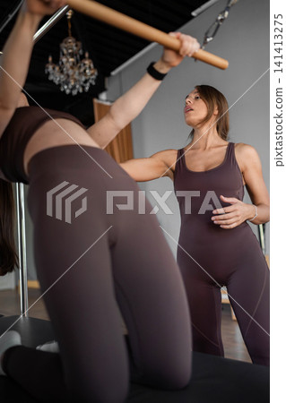 Elegant pilates pair performing synchronized deep stretches using reformer beds in bright wood-floored studio. Synchronized, deep stretch, reformer, studio, wood floor Elegant pilates pair performing synchronized deep stretches using reformer beds in bright wood-floored studio. Synchronized, deep stretch, reformer, studio, wood floor 141413275