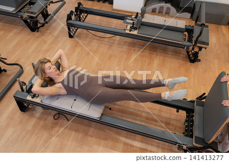 Woman training pilates with trainer on the reformer bed. Reformer pilates studio machine for fitness workouts in gym. Fit, healthy and strong authentical body. Fitness Woman training pilates with trainer on the reformer bed. Reformer pilates studio machine for fitness workouts in gym. Fit, healthy and strong authentical body. Fitness 141413277