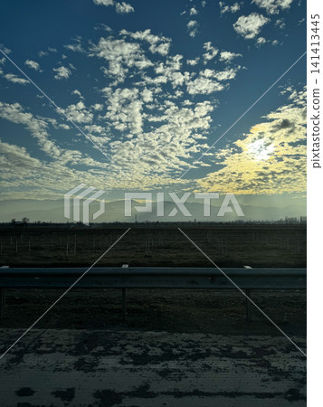 Field and mountain silhouette under cloudy blue sky at sunrise with road in foreground. Field and mountain silhouette under cloudy blue sky at sunrise with road in foreground. 141413445