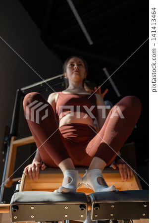 Foot work and core exercise on a Pilates Reformer machine illuminated by sunlight. Fit, healthy and strong authentical body. Fitness concept. Foot work and core exercise on a Pilates Reformer machine illuminated by sunlight. Fit, healthy and strong authentical body. Fitness concept. 141413464