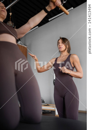Elegant pilates pair performing synchronized deep stretches using reformer beds in bright wood-floored studio. Synchronized, deep stretch, reformer, studio, wood floor Elegant pilates pair performing synchronized deep stretches using reformer beds in bright wood-floored studio. Synchronized, deep stretch, reformer, studio, wood floor 141413494