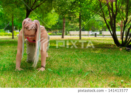 Yoga instructor demonstrating cat-cow pose on mat outdoors in green summer park for students. Cat-cow pose, yoga, instructor, mat, summer, outdoors. Yoga instructor demonstrating cat-cow pose on mat outdoors in green summer park for students. Cat-cow pose, yoga, instructor, mat, summer, outdoors. 141413577