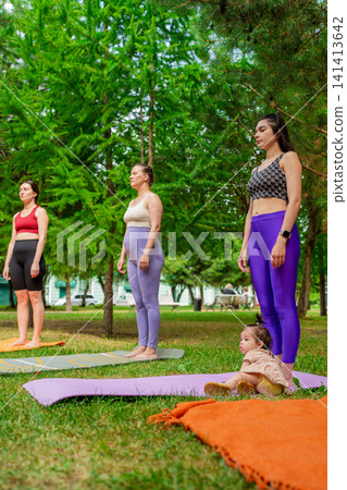 Ladies in purple leggings and green tops standing and stretching before group yoga class in summer park. Purple leggings, stretching, group, yoga, park. Ladies in purple leggings and green tops standing and stretching before group yoga class in summer park. Purple leggings, stretching, group, yoga, park. 141413642