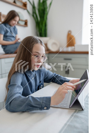 Girl with tablet sitting on kitchen counter and reading digital book in cheerful mood. Tablet, digital, kitchen, girl, reading. Girl with tablet sitting on kitchen counter and reading digital book in cheerful mood. Tablet, digital, kitchen, girl, reading. 141413808