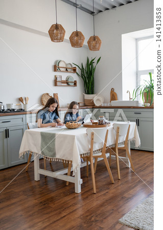 Casual girls seated and eating breakfast at modern kitchen table with notepads and drinks. Breakfast, kitchen, eating, girls, notepads, drinks. Casual girls seated and eating breakfast at modern kitchen table with notepads and drinks. Breakfast, kitchen, eating, girls, notepads, drinks. 141413858