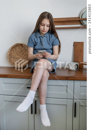 Young girl sitting on kitchen counter with book looking thoughtful in modern home. Kitchen, book, counter, thoughtful, girl, modern. 141413863