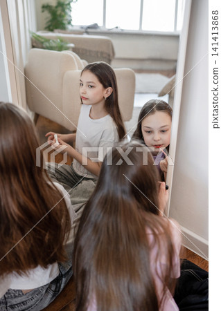 Two girls sitting on bed looking at mirror and applying face makeup in bright modern bedroom. Bed, girls, mirror, makeup, bedroom, bright. Two girls sitting on bed looking at mirror and applying face makeup in bright modern bedroom. Bed, girls, mirror, makeup, bedroom, bright. 141413868