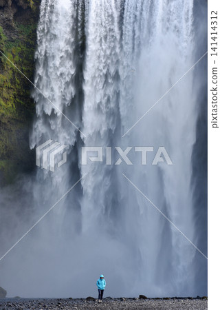 Hiker standing before the immense Skogafoss waterfall, Iceland 141414312