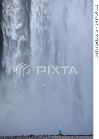 A hiker standing below the towering Skogafoss waterfall, Iceland A hiker standing below the towering Skogafoss waterfall, Iceland 141414313