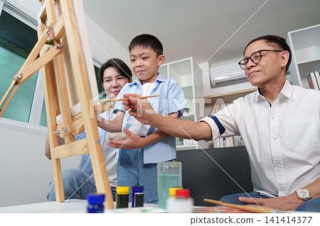 Asian grandfather teaching grandson to paint on easel with father at home Asian grandfather teaching grandson to paint on easel with father at home 141414377