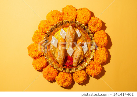 Diwali festive thali with traditional Indian sweets and marigold flowers on yellow background Diwali festive thali with traditional Indian sweets and marigold flowers on yellow background 141414401