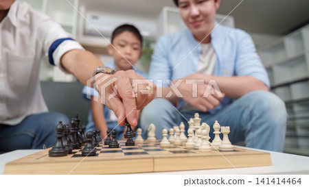Asian multigenerational family playing chess at home for strategic learning 141414464