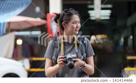 Young Asian woman traveler with backpack and camera exploring city street Young Asian woman traveler with backpack and camera exploring city street 141414466
