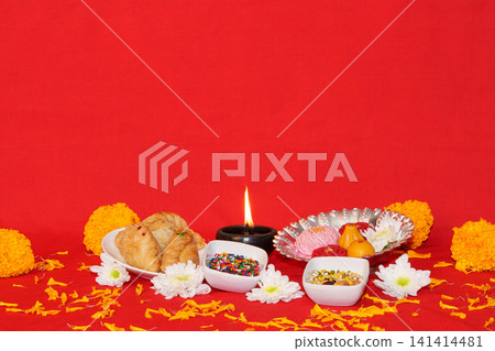 Traditional Diwali sweets and lit clay diya lamp on red background Traditional Diwali sweets and lit clay diya lamp on red background 141414481