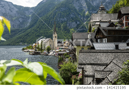 Hallstatt village with traditional alpine buildings lining the waterfront, illustrating authentic landscape and summer tourism. Hallstatt village with traditional alpine buildings lining the waterfront, illustrating authentic landscape and summer tourism. 141415195