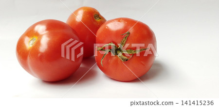 A close-up photo of three fresh red tomatoes on a white surface. 141415236