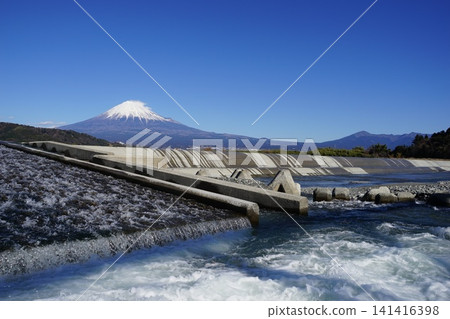 With Mount Fuji standing out against the blue sky in the background, a scene of water spraying in front of the dam. January, Mount Fuji 2147 Fujikawa Dam and water spray 141416398
