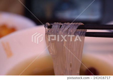 Chopsticks Holding Translucent Noodles Over Soup Chopsticks Holding Translucent Noodles Over Soup 141416717