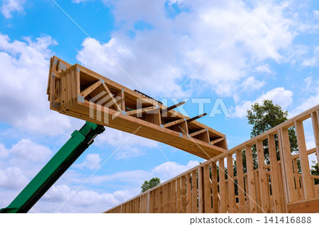 Construction crew uses crane machine to lift wooden trusses beams onto building frame Construction crew uses crane machine to lift wooden trusses beams onto building frame 141416888