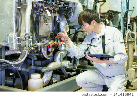 A young Japanese male worker inspects machinery while holding a tablet. Photo courtesy of Denpa Gakuen Educational Foundation, Tokyo Electronics College. A young Japanese male worker inspects machinery while holding a tablet. Photo courtesy of Denpa Gakuen Educational Foundation, Tokyo Electronics College. 141416941
