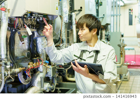 A young Japanese male worker inspects machinery while holding a tablet. Photo courtesy of Denpa Gakuen Educational Foundation, Tokyo Electronics College. A young Japanese male worker inspects machinery while holding a tablet. Photo courtesy of Denpa Gakuen Educational Foundation, Tokyo Electronics College. 141416943