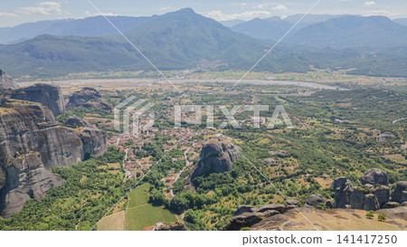 Panoramic drone shot of Meteora rock pillars and Kastraki village in valley with distant mountain range under blue sky in Thessaly region Greece in summer 141417250