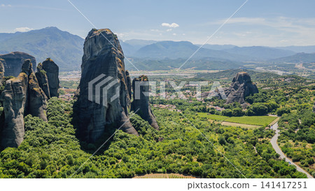 Drone view of massive Meteora rock formations near Kastraki village in Thessaly Greece surrounded by dense green forest on sunny summer day under blue sky 141417251