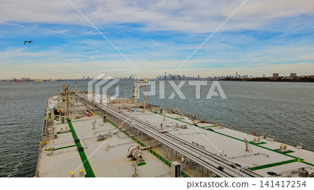 High angle view from oil tanker vessel deck moving in bay with urban city skyline on horizon background during sunny day for maritime transport industry High angle view from oil tanker vessel deck moving in bay with urban city skyline on horizon background during sunny day for maritime transport industry 141417254