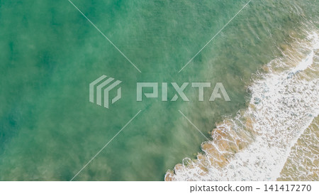 Top down drone shot of emerald green sea water and white foamy waves crashing on sandy shore background in tropical coastal paradise location during summer Top down drone shot of emerald green sea water and white foamy waves crashing on sandy shore background in tropical coastal paradise location during summer 141417270