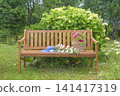 Blue hat, wicker basket with summer vegetable on a wooden bench in a blooming summer garden 141417319