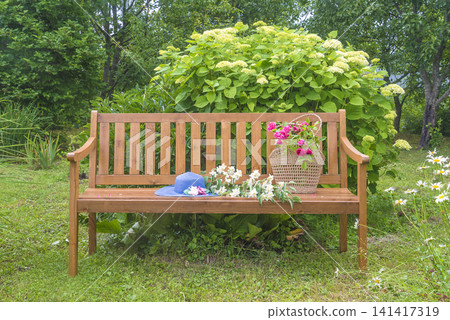 Blue hat, wicker basket with summer vegetable on a wooden bench in a blooming summer garden 141417319
