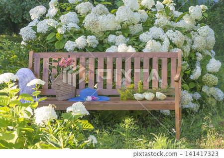 Blue hat, wicker basket with summer vegetable on a wooden bench in a blooming summer garden 141417323