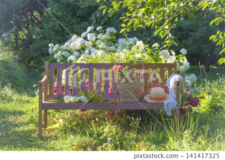 Blue hat, wicker basket with summer vegetable on a wooden bench in a blooming summer garden 141417325