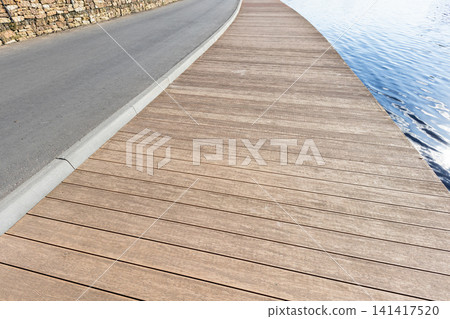 Empty wooden boardwalk runs beside a calm waterfront Empty wooden boardwalk runs beside a calm waterfront 141417520
