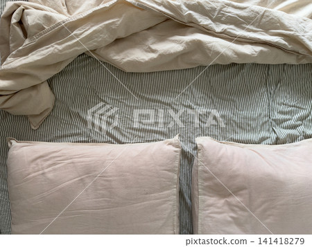 Cream and pink pillows with rumpled duvet on a striped sheet, top view Cream and pink pillows with rumpled duvet on a striped sheet, top view 141418279