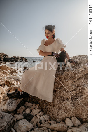 Woman dress cat smiling lady in vintage white gown sitting on a coastal rock with her black pet Woman dress cat smiling lady in vintage white gown sitting on a coastal rock with her black pet 141418313
