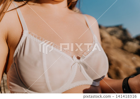 Woman white bra lace lingerie standing outdoors under bright sunlight during a summer afternoon Woman white bra lace lingerie standing outdoors under bright sunlight during a summer afternoon 141418316