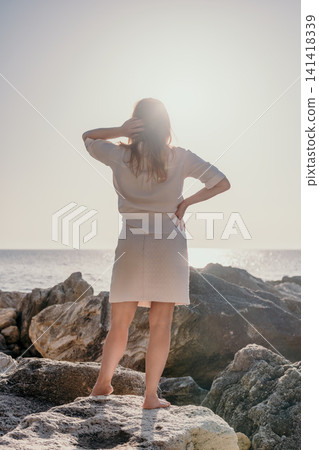 Woman beach ocean standing on rocky shore looking at the sea under bright sunlight with copy space in the sky Woman beach ocean standing on rocky shore looking at the sea under bright sunlight with copy space in the sky 141418339
