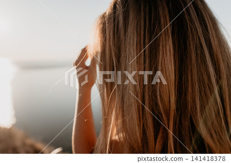 Hair woman sunset backlit view of a female looking at the calm sea during golden hour to capture a sense of peaceful solitude Hair woman sunset backlit view of a female looking at the calm sea during golden hour to capture a sense of peaceful solitude 141418378
