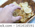A hand picking up potato chips and a wooden bowl A hand picking up potato chips and a wooden bowl 141418591