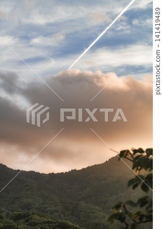 A straight contrail stretches across the sky and mountain range, bathed in the colors of the setting sun. A straight contrail stretches across the sky and mountain range, bathed in the colors of the setting sun. 141419489
