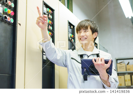 A young Japanese male worker inspects a control panel with a tablet. Photo courtesy of Denpa Gakuen Educational Foundation, Tokyo Electronics College. A young Japanese male worker inspects a control panel with a tablet. Photo courtesy of Denpa Gakuen Educational Foundation, Tokyo Electronics College. 141419836