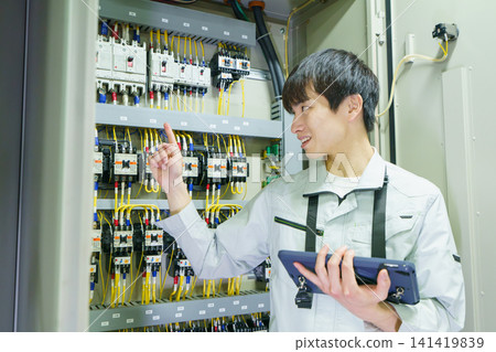 一名年輕的日本男工作者正在用平板電腦檢查控制面板。照片由東京電子大學電波學園教育基金會提供。 一名年輕的日本男工作者正在用平板電腦檢查控制面板。照片由東京電子大學電波學園教育基金會提供。 141419839