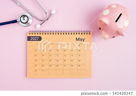 May 2027 desk calendar and stethoscope with piggy bank. Savings for Health concept. 141420347