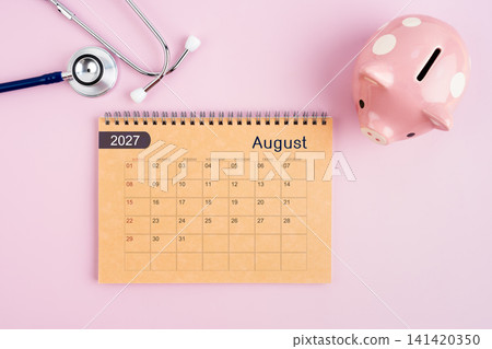 August 2027 desk calendar and stethoscope with piggy bank. Savings for Health concept. August 2027 desk calendar and stethoscope with piggy bank. Savings for Health concept. 141420350