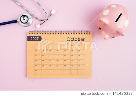 October 2027 desk calendar and stethoscope with piggy bank. Savings for Health concept. October 2027 desk calendar and stethoscope with piggy bank. Savings for Health concept. 141420352