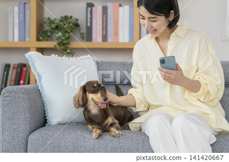 一位年輕女子拿著智慧型手機撫摸著她的狗。 141420667