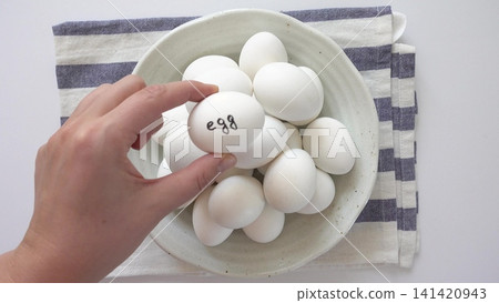 Woman's hand and a ceramic bowl with white eggs on a striped kitchen napkin. Healthy eating, keto and paleo diet Woman's hand and a ceramic bowl with white eggs on a striped kitchen napkin. Healthy eating, keto and paleo diet 141420943